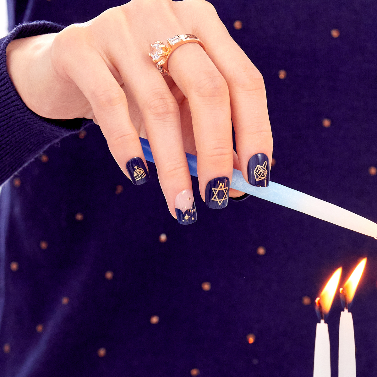 A hand displaying imPRESS Hannukah inspired nails with Dark blue backgrounds and varying holiday designs